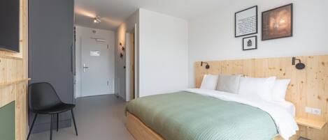 Un dormitorio con cabecera de madera, colcha verde, silla negra y dos cuadros en la pared.