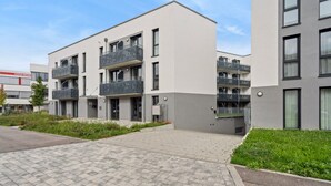 Un edificio residencial moderno de varios pisos con balcones, un sendero pavimentado y un césped bien cuidado.