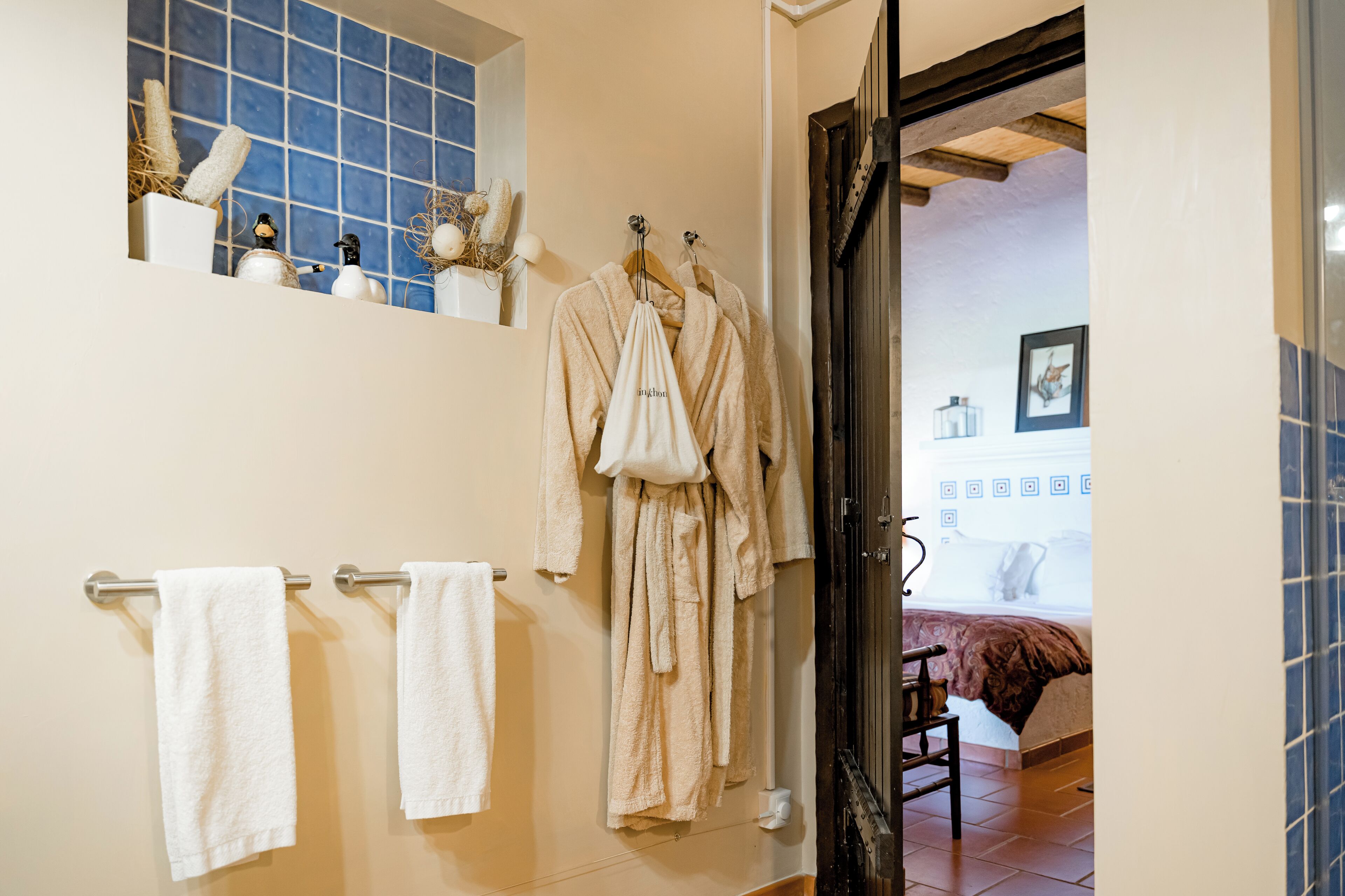 A bathroom with white towels, a rack, and a wooden door leading to a bedroom.