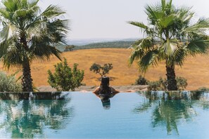 A pool with clear water, surrounded by palm trees and a view of a dry landscape. - Vale do Manantio, the ideal hideaway to spend unforgettable and unique days! (Povoa São Miguel)