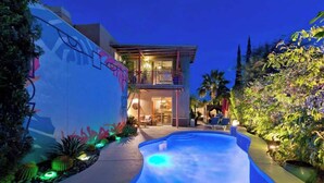 A modern house with a swimming pool, a balcony, and a well-lit exterior.
