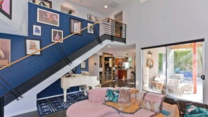 A modern living room with a curved pink sofa, a staircase with black railings, and a large window offering a view of the outdoors.
