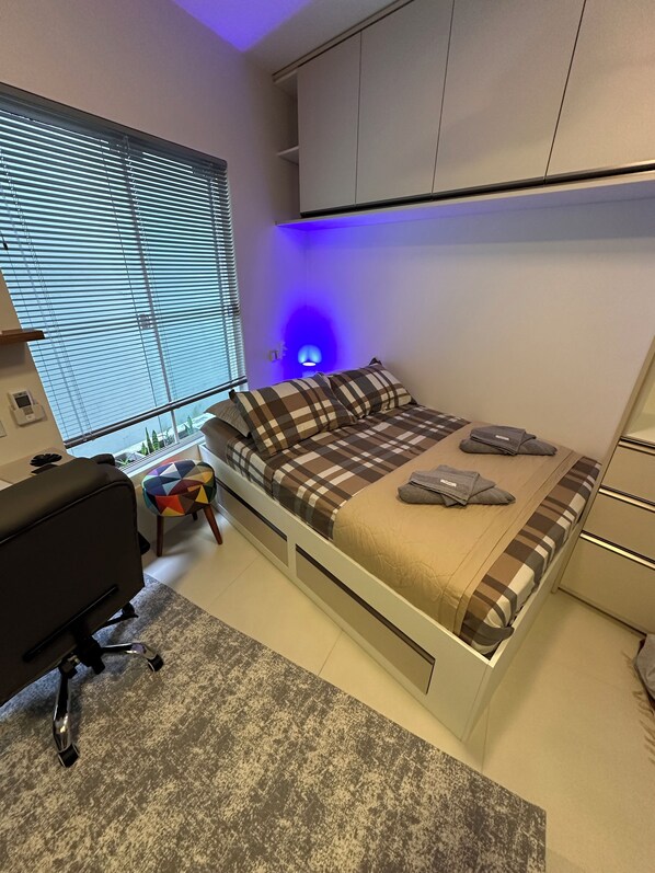 A bedroom with a bed, a desk, a chair, and a window with blinds. - Beautiful and complete loft in Fazenda (Fazenda Itajaí)