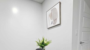 A conference room with a round table, four black chairs, a vase with green plants, and a framed abstract painting on the wall.