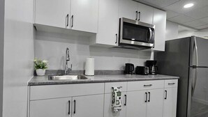 A modern kitchen with white cabinets, stainless steel appliances, and a wooden floor.