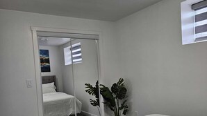 A hotel room with a large bed, a mirror, a potted plant, and a window with blinds.