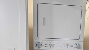 A compact, white front-loading washer and dryer unit with a control panel featuring multiple settings and a red warning label.