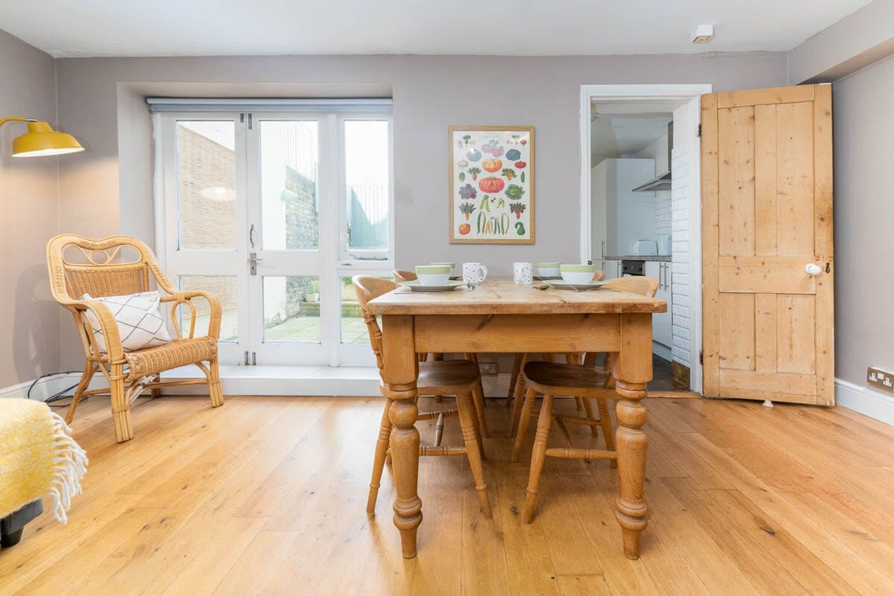 A dining area with a wooden table and chairs, a wicker chair, and a painting on the wall.