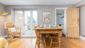 A dining area with a wooden table and chairs, a wicker chair, and a painting on the wall. - Host Stay Waterloo Apartment (Hove)