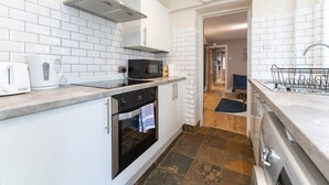 A modern kitchen with white tiled walls, a built-in oven, a microwave, and a stainless steel range hood. - Host Stay Waterloo Apartment (Hove)