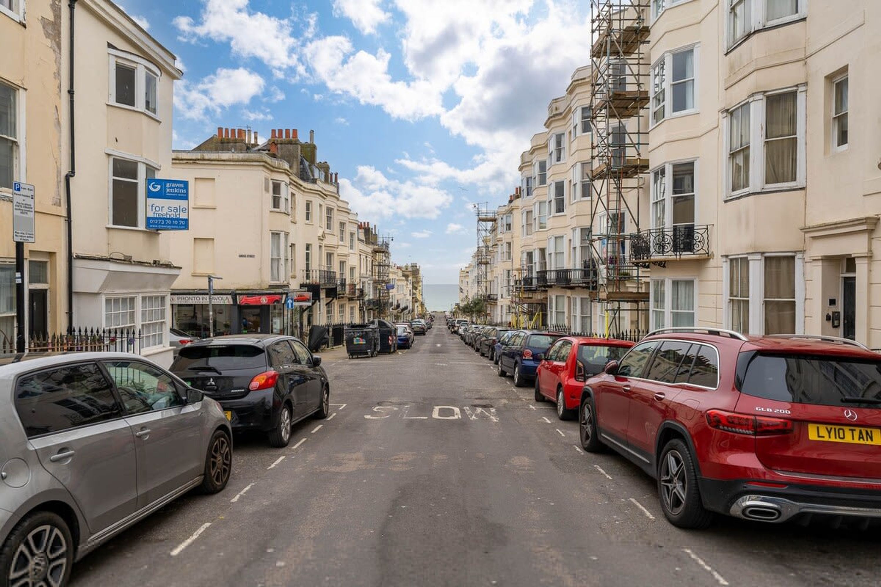 A street lined with parked cars and buildings, including a 'for sale' sign and a 'Priority in Avoca' sign.