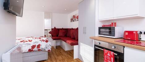 Una habitación funcional con cama, sofá, kitchenette y televisión.
