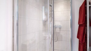 Une douche fermée par des parois en verre, dotée d’un pommeau de douche à main et d’un robinet mural.