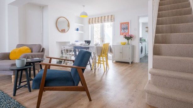 Uma sala de estar moderna com uma poltrona azul, uma área de jantar e uma escada.