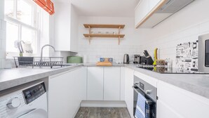 Uma cozinha moderna com armários brancos, máquina de lavar louça embutida e diversos eletrodomésticos.