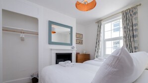 Quarto de hotel com cama, espelho, lareira, guarda-roupa e janela com cortinas.