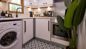 Una cucina moderna con mobili bianchi, lavatrice integrata, forno in acciaio inossidabile e una finestra con cornice in legno.