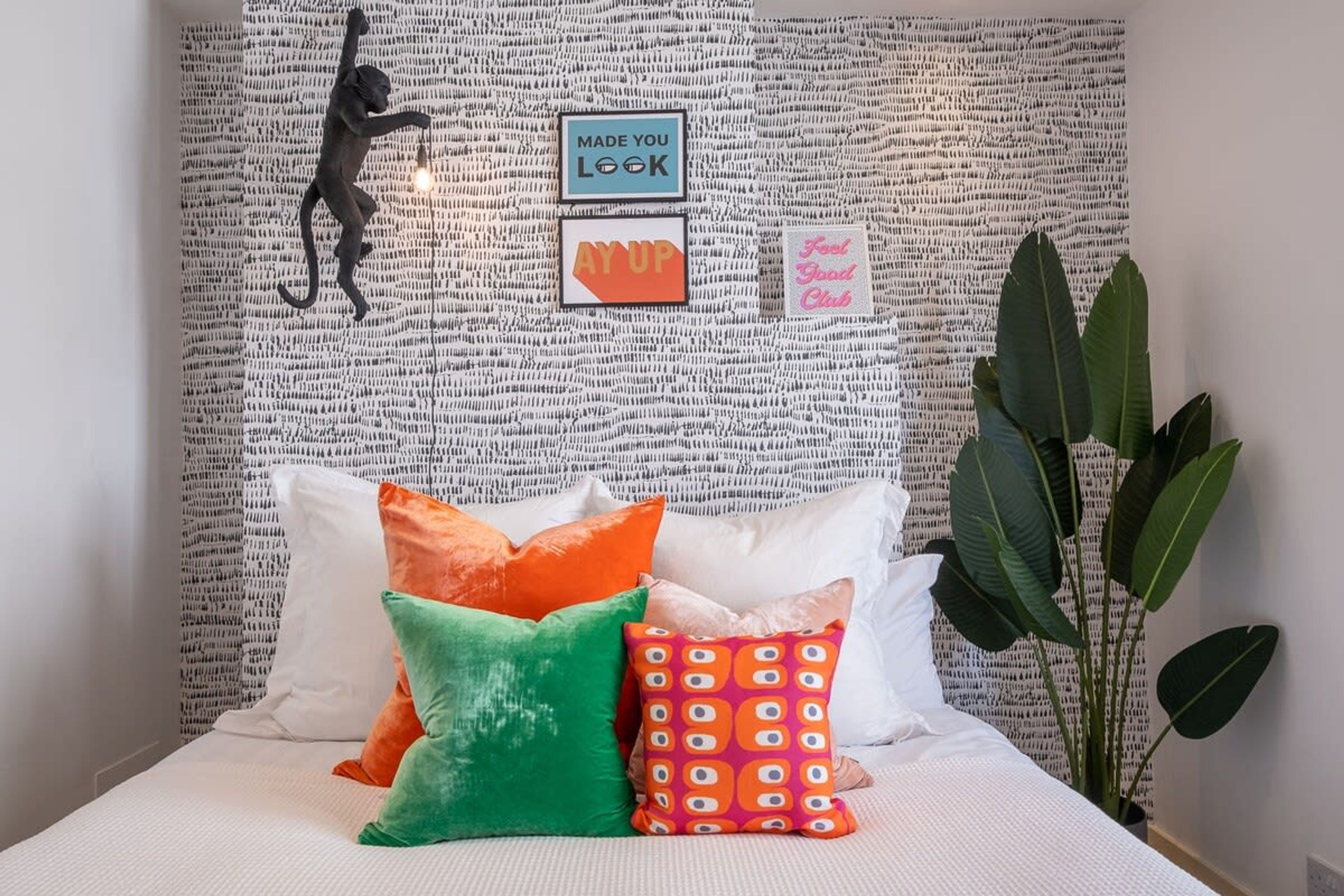 A bed with colorful pillows, a wall tapestry, and a plant.