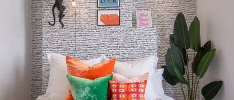 A bed with colorful pillows, a wall tapestry, and a plant.