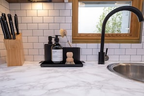 A kitchen with a marble countertop, a wooden knife block, a soap dispenser, and a faucet. - Host Stay The Brighton Breeze (Brighton)