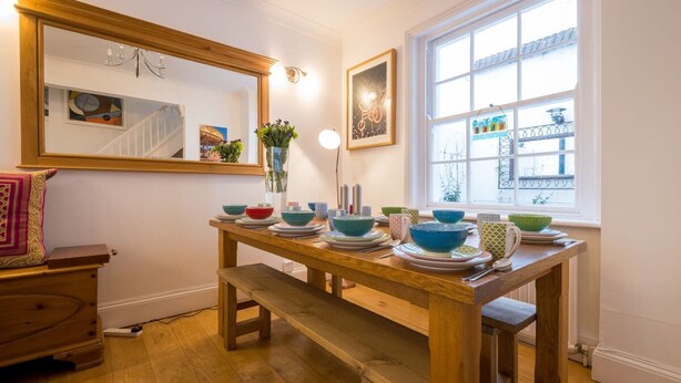 A dining area with a wooden table set with bowls and plates, a bench, and a large window with a view of the outside. - Host Stay Over Arches (Brighton)