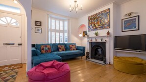 A living room with a blue sofa, a pink bean bag, a fireplace, and a TV. - Host Stay Over Arches (Brighton)