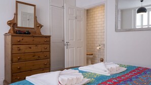 A bedroom with a bed, a wooden dresser, a mirror, and a door leading to a bathroom. - Host Stay Over Arches (Brighton)