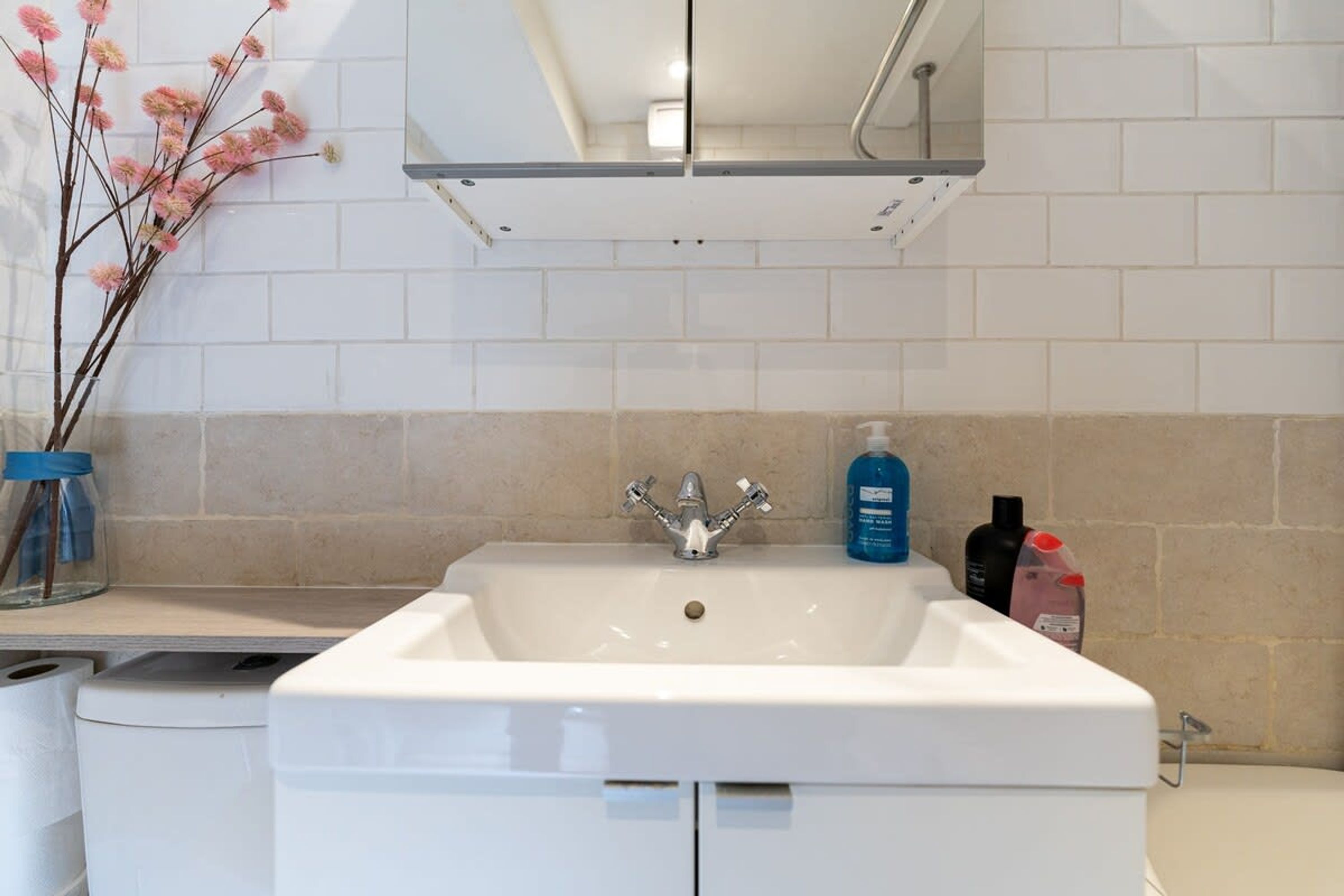 A bathroom with a white sink, a mirror above it, and toiletries on the counter.