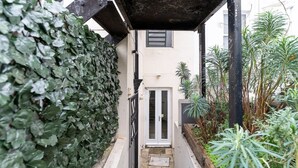 A narrow alleyway with a white door, a black gate, and a wall covered in ivy. - Host Stay Seven Dials Apartment (Brighton)