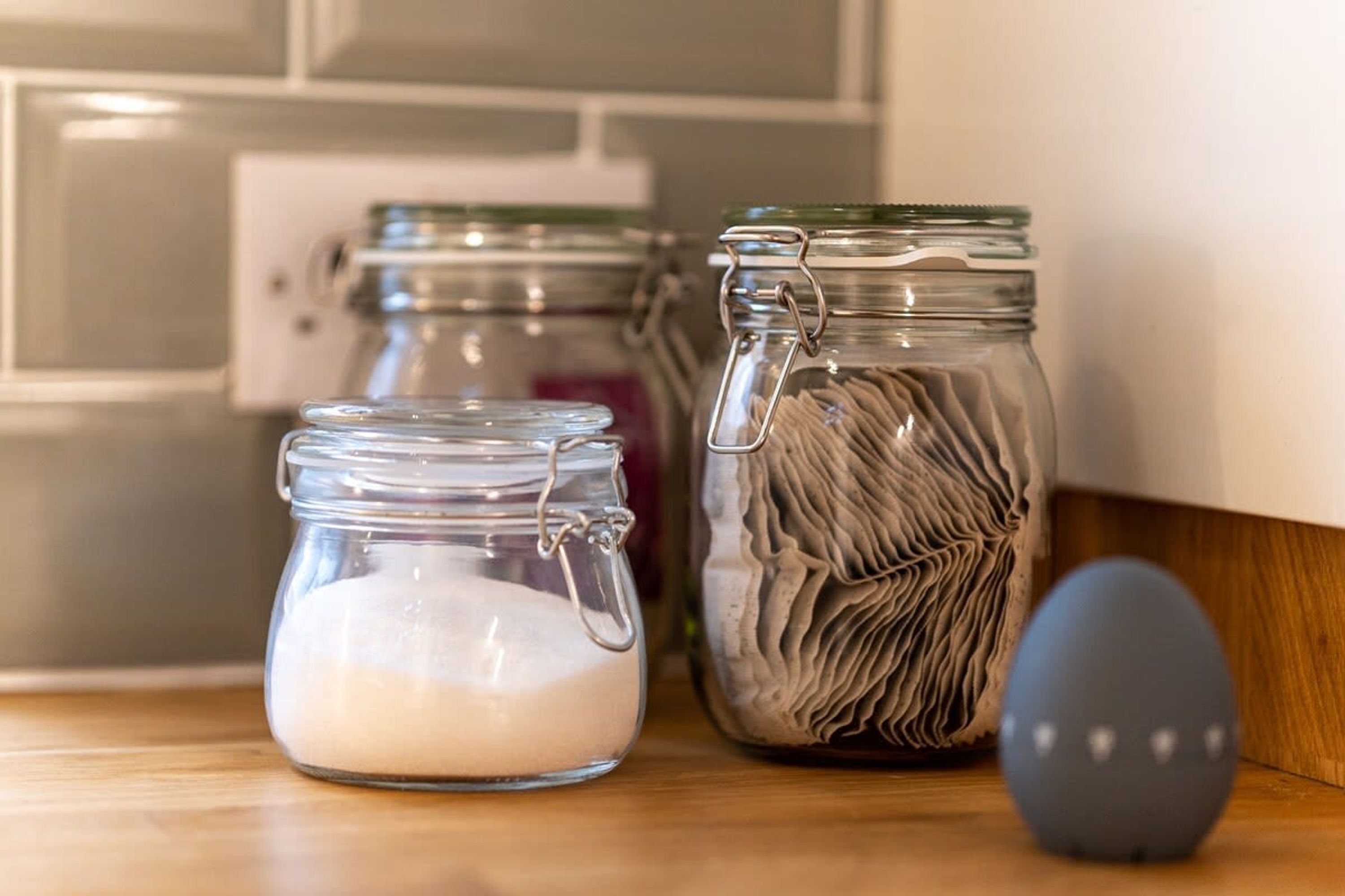 Three glass jars on a wooden surface, one with a metal clasp and another with a textured lid.