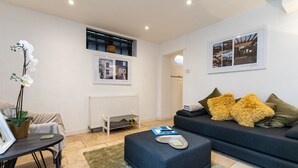 A modern living room with a dark blue sofa, a small ottoman, a potted orchid, and a framed picture on the wall. - Host Stay Seven Dials Apartment (Brighton)
