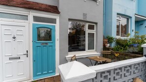 Ein Wohngebäude mit einer weißen Tür, einer blauen Tür und einer kleinen Außen-Sitzgelegenheit mit Tisch und Stühlen.