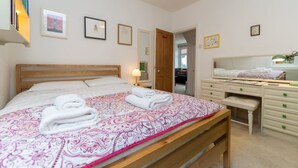 Ein Schlafzimmer mit Bett, Nachttisch, Kommode und einer Tür zu einem weiteren Raum.