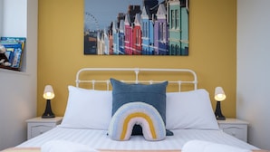A neatly made bed with a rainbow-patterned pillow, white bedding, and a colorful striped blanket. - Host Stay Kingscote Townhouse (Brighton)