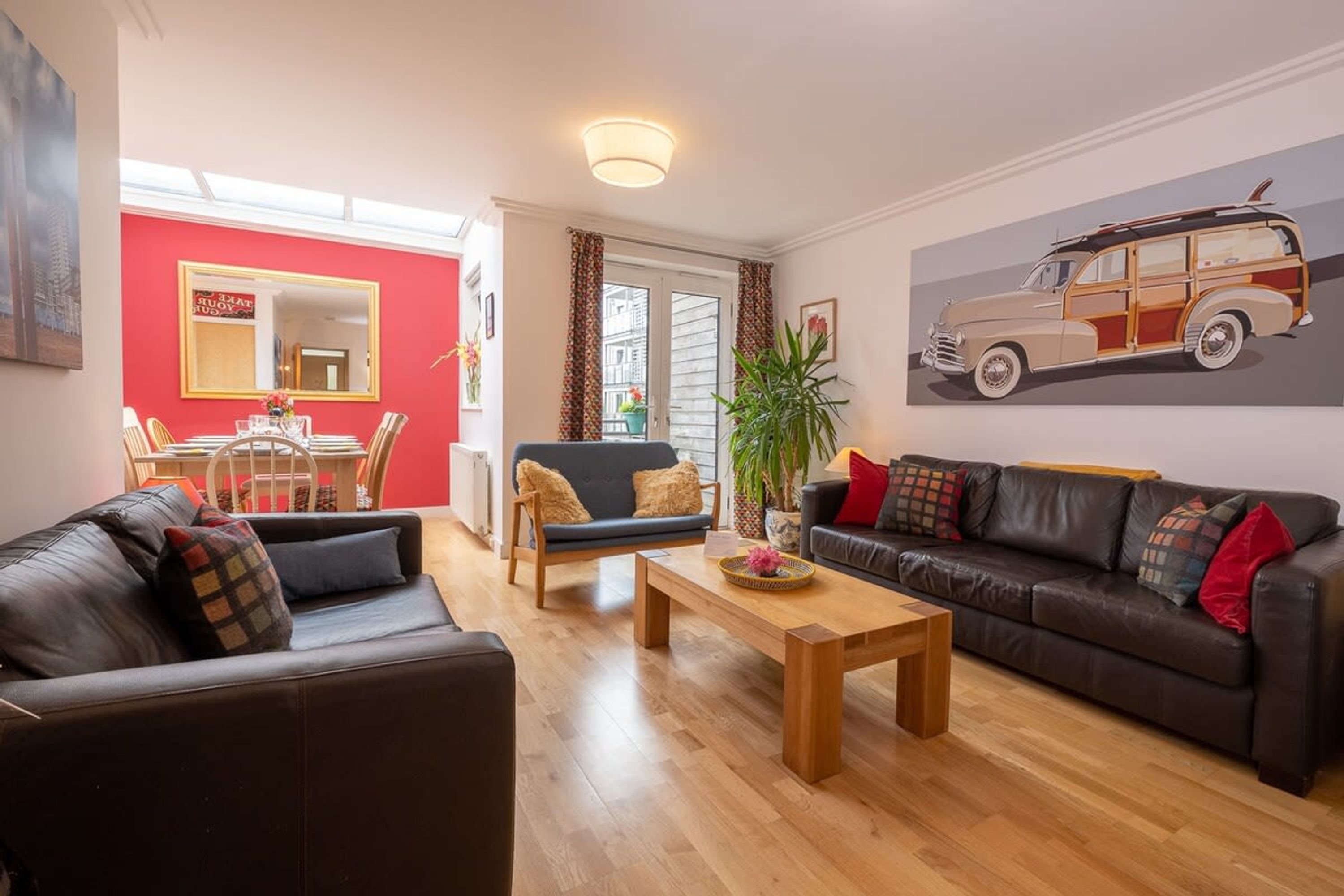 A living room with a black leather sofa, a wooden coffee table, and a red wall with a mirror.