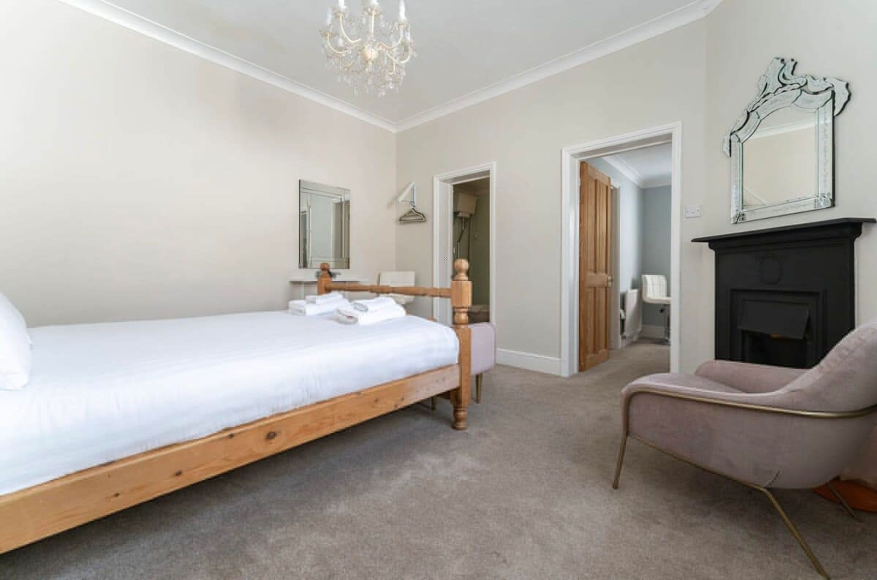 A bedroom with a wooden bed, a chair, a mirror, and a fireplace.
