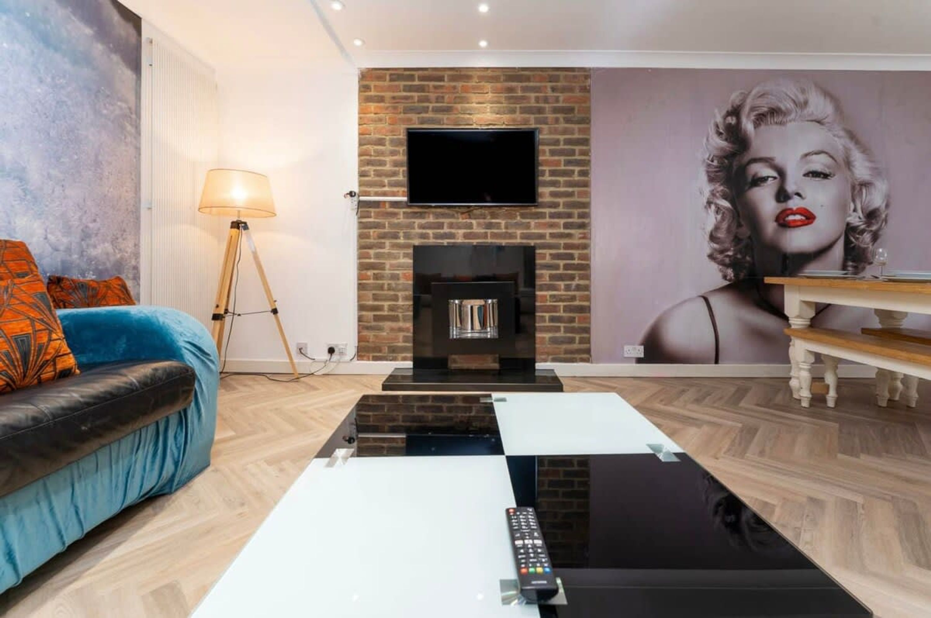 A living room with a brick fireplace, a flat-screen TV, a sofa with orange cushions, a coffee table, and a lamp.