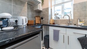 A modern kitchen with grey tiles, a black countertop, a built-in oven, a sink, and a window with blinds. - Host Stay Round Hill Apartment (Brighton)