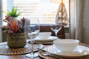A dining table set with white plates, bowls, and wine glasses, with a potted plant and a hanging light fixture in the background. - Host Stay Round Hill Apartment (Brighton)