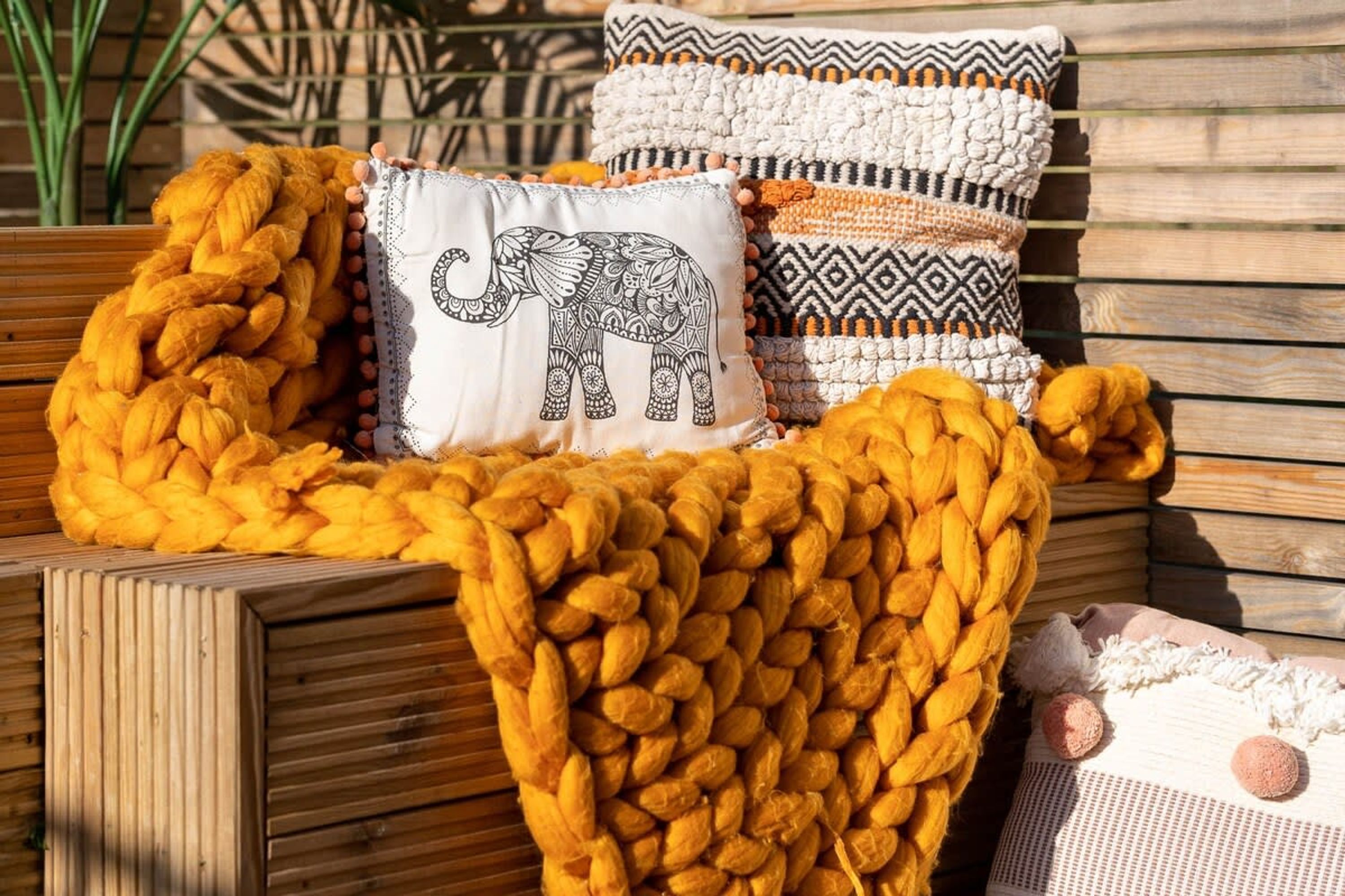Un banco de madera con una manta de punto grueso y almohadones decorativos, incluyendo uno con un diseño de elefante.