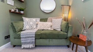 A green sofa with patterned cushions, a round mirror, and a small table with a welcome sign. - Host Stay Round Hill Apartment (Brighton)