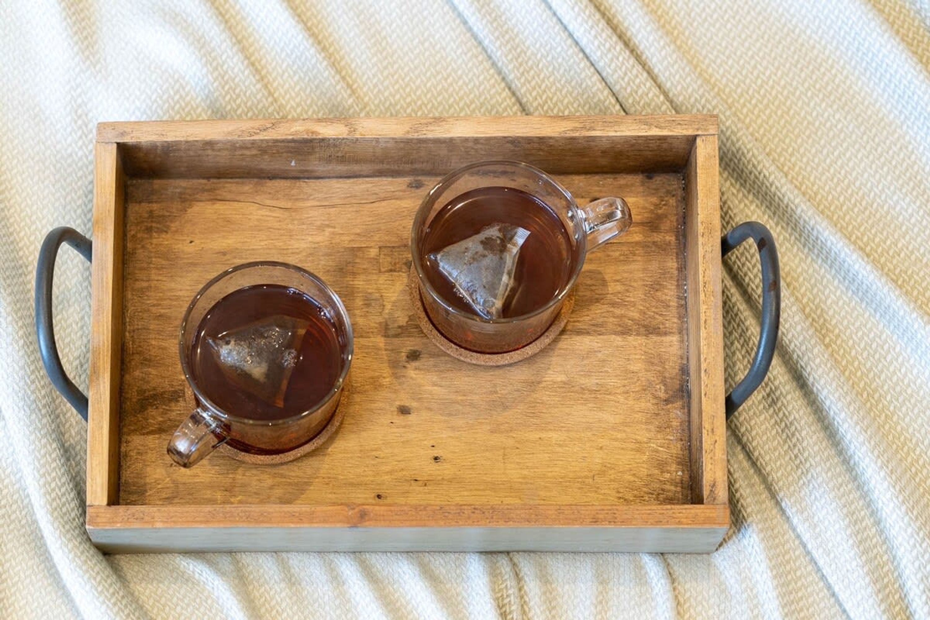 A wooden tray with two glass cups of tea.