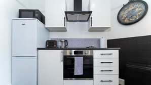 Eine kompakte Küche mit einem weißen Kühlschrank, einer Mikrowelle, einem Herd und einer Wanduhr.