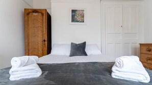 Ein ordentlich bezogenes Bett mit weißer und grauer Bettwäsche, einer grauen Decke und zwei Handtüchern auf jeder Seite.