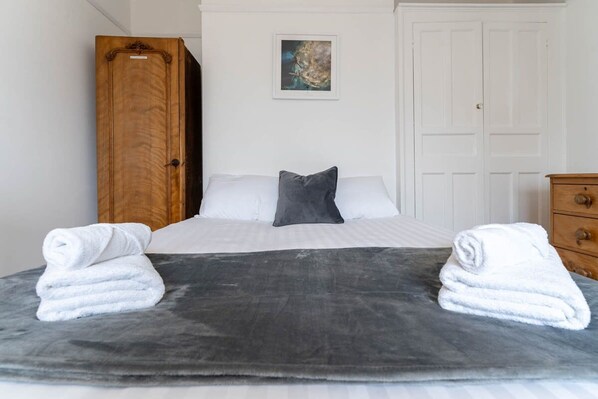 A neatly made bed with white and gray linens, a gray blanket, and two towels on either side. - Host Stay Preston Park Apartment (Brighton)
