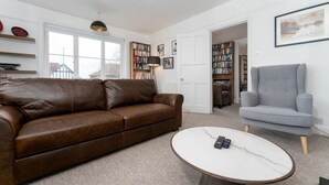 Ein Wohnzimmer mit einem braunen Ledersofa, einem grauen Sessel, einem weißen Marmortisch und einem Bücherregal voller Bücher.