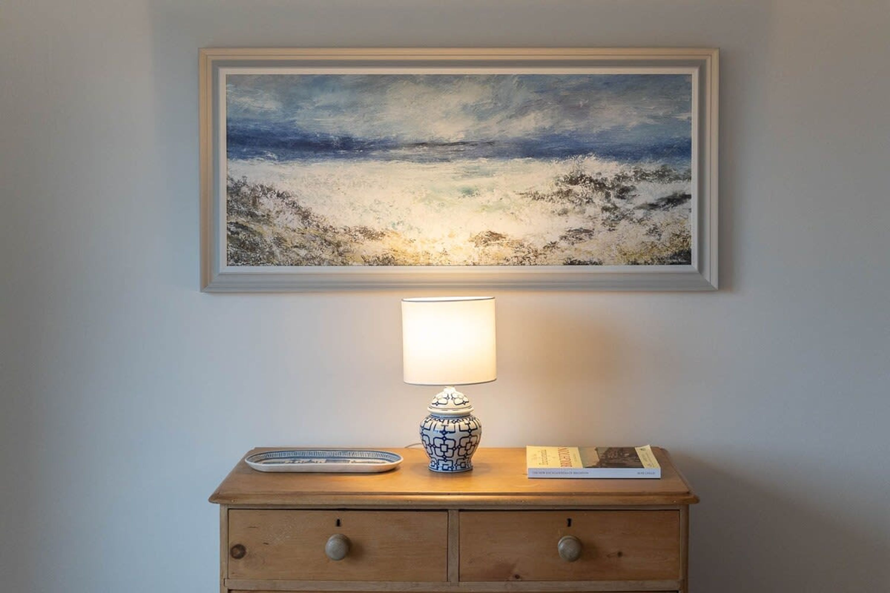 A wooden nightstand with a lamp and a framed painting above it.