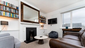 Ein Wohnzimmer mit Kamin, Bücherregalen, Fernseher und großem Fenster.