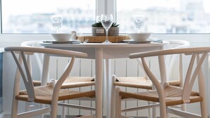 A round dining table with four white chairs, each with a woven seat. The table is set with two bowls, two wine glasses, and a small potted plant. - Host Stay Sea View on Manchester Road (Brighton)