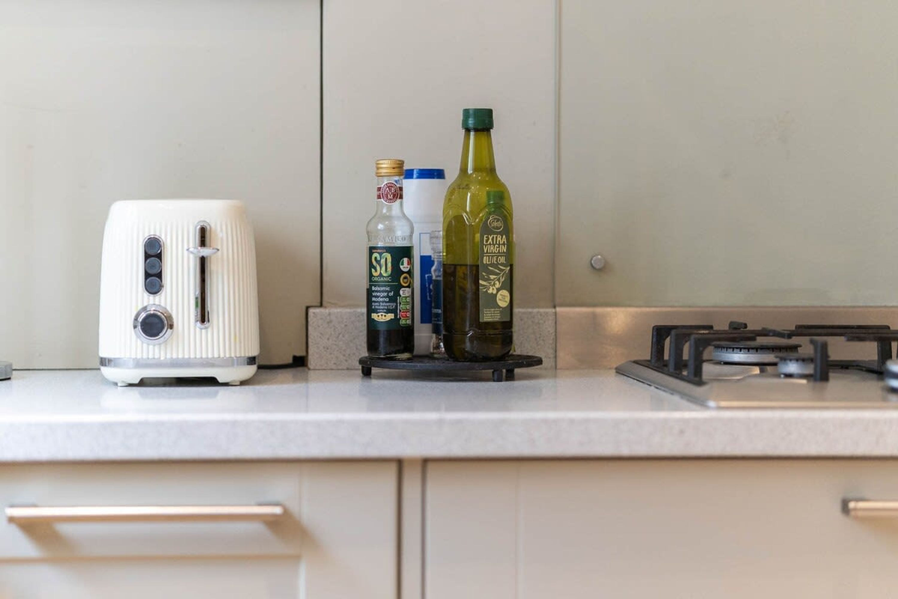 A kitchen counter with a white toaster, a bottle of extra virgin olive oil, and a bottle of organic vodka.